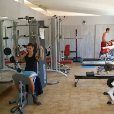 Salle de sport avec équipements de musculation et un homme utilisant une machine de fitness.
