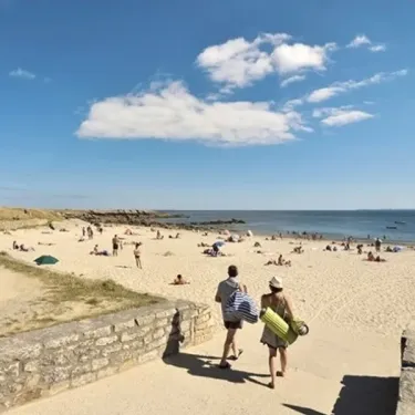 Promenade sur une plage animée au Camping Bois d'Amour, avec mer et ciel bleu.