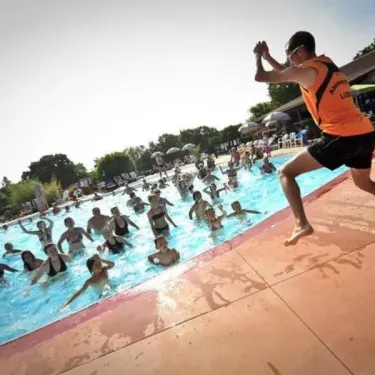 Camping Les Cigales : surveillant en orange sautant dans la piscine avec des enfants.