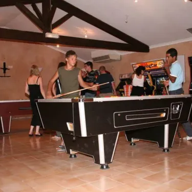 Camping Le Grand Calme : groupe jouant au billard dans une salle avec piste de jeux vidéo.