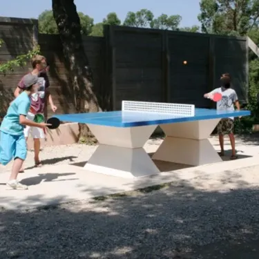Enfants jouant au ping-pong à l'extérieur sur une table bleue et blanche, Camping Le Grand Calme.