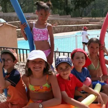 Enfants souriants près d'une piscine avec flotteurs colorés, Camping Le Grand Calme.