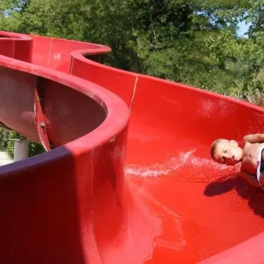 Enfant glissant sur une grande slide rouge au Camping Le Céou
