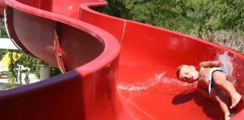 Enfant glissant sur une grande slide rouge au Camping Le Céou