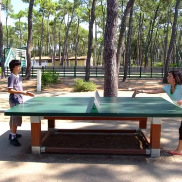 Deux enfants jouent au ping-pong à Camping La Plage de Riez sous les pins.