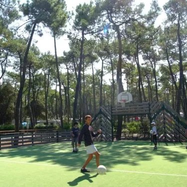 Enfant joue au basket-ball sur un terrain vert dans le camping La Plage de Riez.