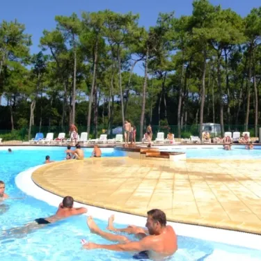 Camping La Plage de Riez : piscine avec des visiteurs et pins en arrière-plan.