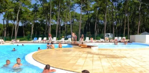 Camping La Plage de Riez : piscine avec des visiteurs et pins en arrière-plan.