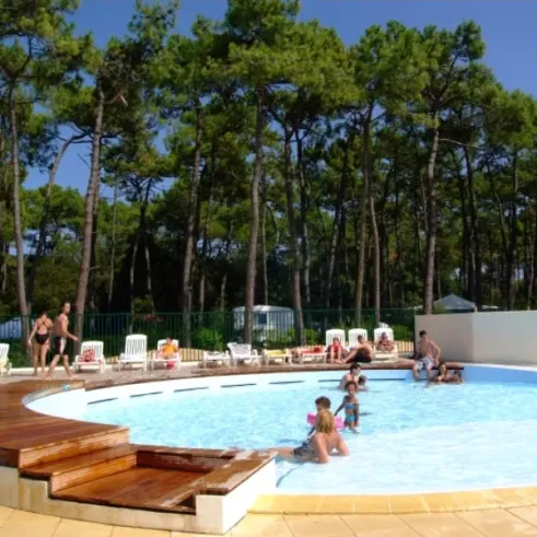 Piscine extérieure entourée d'arbres, avec des personnes qui nagent ou se détendent sur les chaises longues.