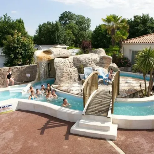 Piscine avec chute d'eau artificielle et enfants nageant autour, au Camping La Grand Métairie.