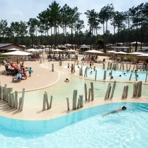 Piscine en plein air du Camping Fram Nature entourée d'arbres, avec des enfants qui nagent et des adultes qui se détendent.