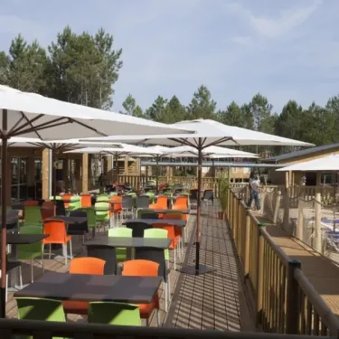Terrasse avec tables et chaises colorées sous parasols blancs au Camping Fram Nature