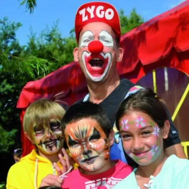 Clown ZYGO peignant les visages d'enfants devant une tente rouge, Camping Azu'Rivage