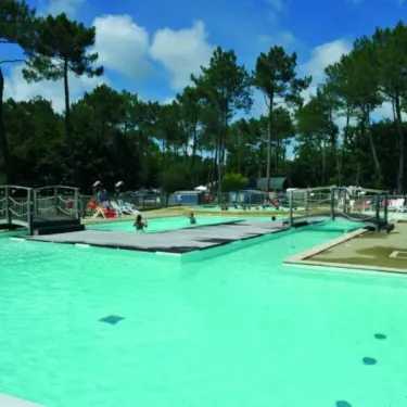 Piscine avec enfants nageant, bord de piscine avec parasols et cabanes en bois, Camping Azu'Rivage