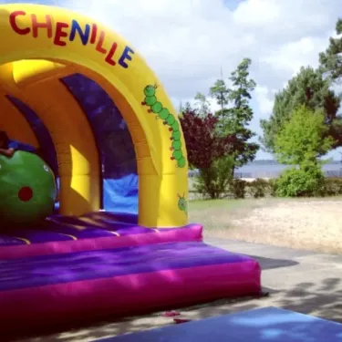 Arc de jeu gonflable La Chenille avec un personnage vert et des arbres en arrière-plan.