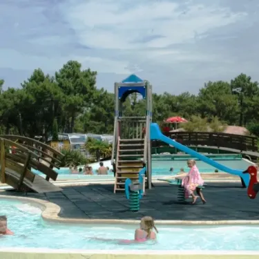 Enfants jouant dans une piscine avec structures de jeux et pont en bois au Camping La Côte d'Argent