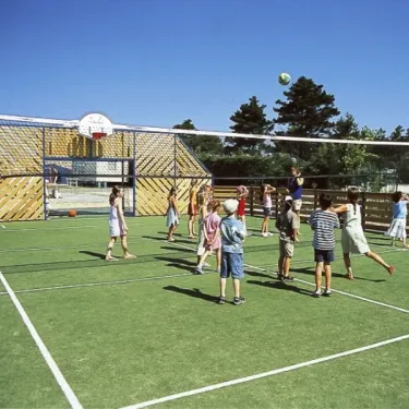 Enfants jouant au volley-ball sur un terrain synthétique entouré d'une clôture en bois