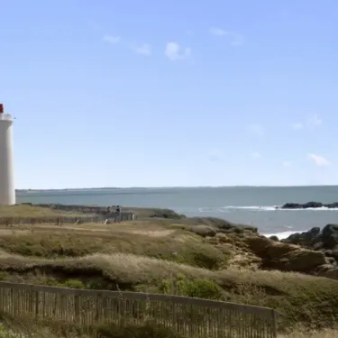 Camping Les Cyprès : phare blanc sur rivage rocheux sous ciel bleu