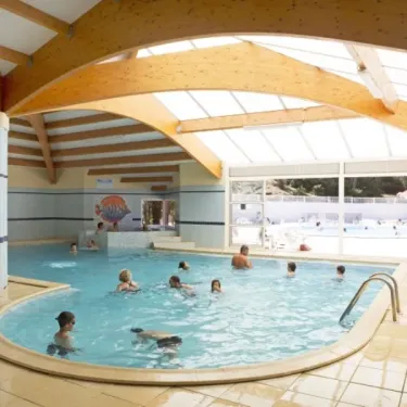 Piscine intérieure couverte du Camping Les Cyprès avec un toit en bois et des visiteurs dans l'eau.