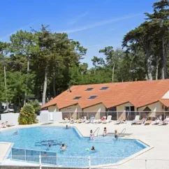 Piscine entourée de chaises longues au Camping Les Cyprès, avec une maison de style campagne à l'arrière.