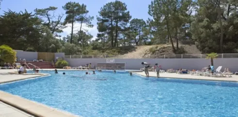 Piscine extérieure du Camping Les Cyprès avec des personnes nageant et des pins en arrière-plan.