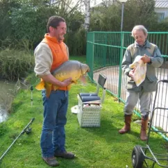 Deux hommes près d'un étang, l'un tenant un grand poisson, Camping Etangs Fleuris