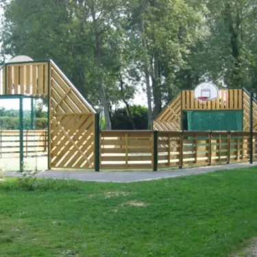 Aire de basket-ball avec panneaux en bois au Camping Etangs Fleuris, entourée d'arbres.