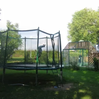 Enfant sautillant sur un trampoline entouré d'une clôture au Camping Etangs Fleuris.