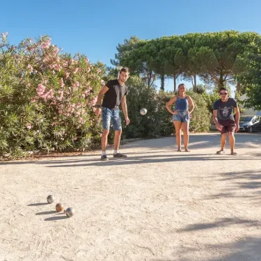 Quatre personnes jouent au boules sur un terrain de sable à Camping L'Occitan.