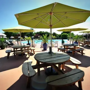 Camping Les Cigales : tables en bois sous parasols jaunes près de la piscine.