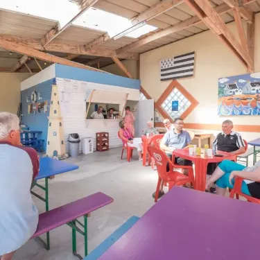 Photo camping Ker Vella : salle de repas avec tables, chaises et drapeau breton.