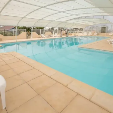 Piscine couverte avec bord de piscine en béton et chaises blanches au Camping Ker Vella