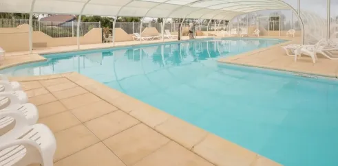 Piscine couverte avec bord de piscine en béton et chaises blanches au Camping Ker Vella