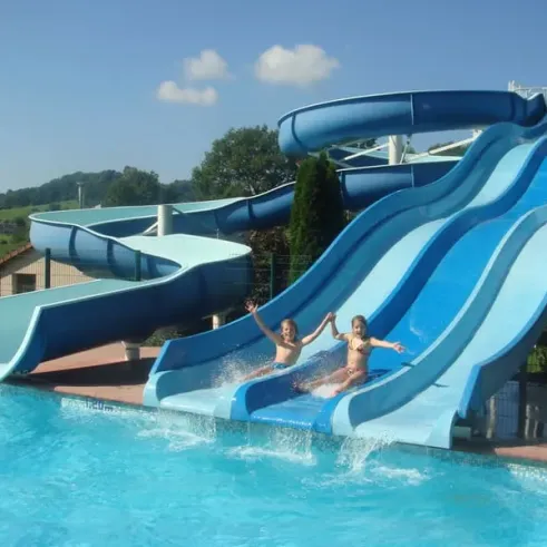 Enfants qui descendent une grande chute d'eau aquatique dans une piscine bleue.