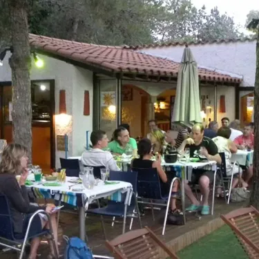 Groupes de personnes dégustent des plats en extérieur devant un restaurant au toit rouge, dans le Camping Val Roma Park.