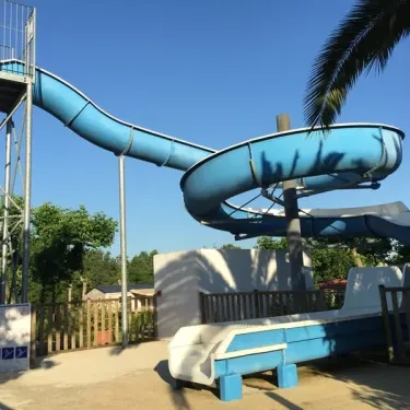 Glissière aquatique bleue au Camping Bela Basque, entourée de palmiers et d'arbres.