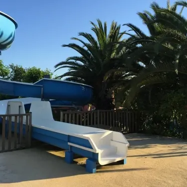 Glissière aquatique bleue et toboggan blanc au Camping Bela Basque, sous palmiers.