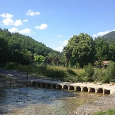 Pont en pierre au-dessus d'un cours d'eau dans le parc du Camping La Bernede.