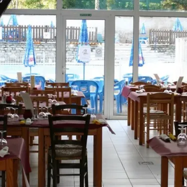 Intérieur d'un restaurant avec tables, chaises et piscine visible à travers la vitre.