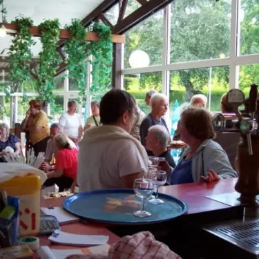 Bar intérieur du camping avec clients et décor végétal suspendu.