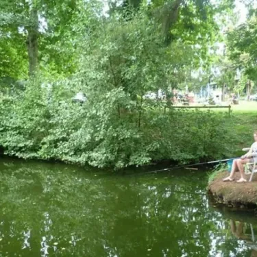 Photo Camping Le Manoir de Bezolle avec personne pêchant sur un étang entouré de verdure.