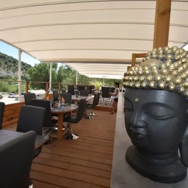 Terrasse extérieure du restaurant avec statue de Bouddha et table en bois