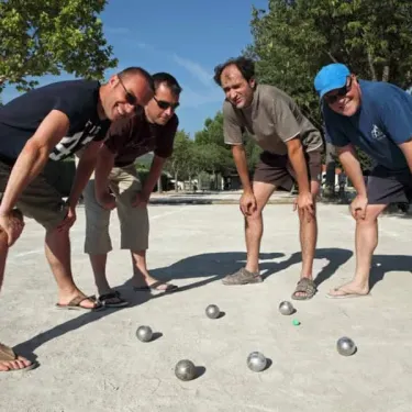 Quatre hommes jouent au bocce sur une cour au Camping Le Chant des Oiseaux