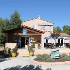 Bureau de Camping La Rivière avec enseigne et terrasse sous parasols