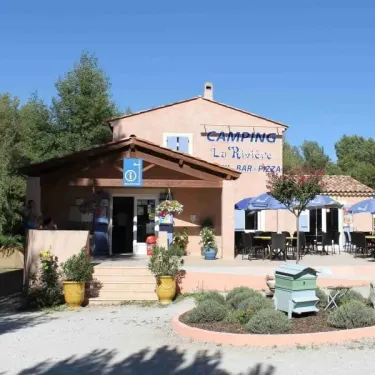 Bureau de Camping La Rivière avec enseigne et terrasse sous parasols