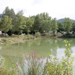 Lac entouré d'arbres avec tentes et caravanes au camping La Rivière