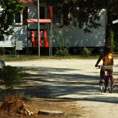 Femme en maillot de bain pédalant un vélo près d'une caravane au Camping Des Pins