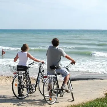 Couple à vélo sur la plage face à l'océan au camping Les Grenettes