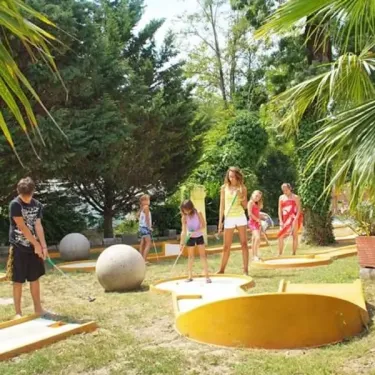 Enfants pratiquent le mini-golf au Camping le Sourire, parmi des palmiers et un jardin verdoyant.