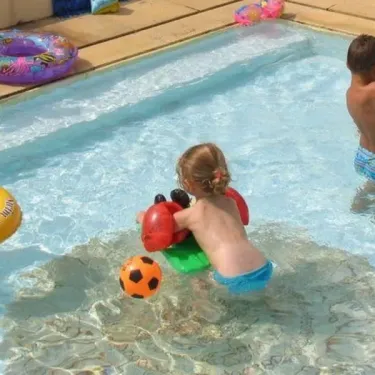 Enfants jouent à la balle dans la piscine du Camping le Sourire, avec flotteurs colorés.